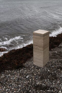 SILO 90, the timeless and elegant pedestal side table in Travertino Classico (travertine) demanding attention at the beach
